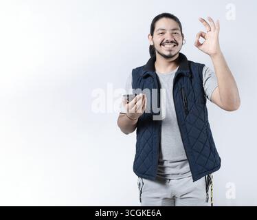 Smiling man gesturing approval with his phone in hand. Young man gesturing approval on the smartphone on isololated Stock Photo