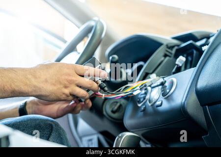 Service technician connecting wires during car dashboard repair, showing vehicle electronics installation, auto maintenance, modern multimedia upgrade, diagnostic process, professional car service. Stock Photo