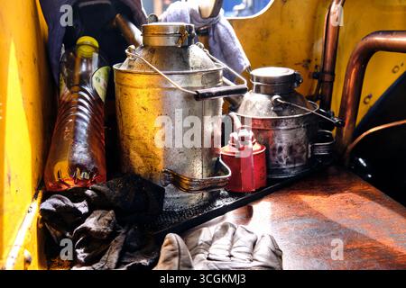 Hoedekenskerke, Netherlands ; May 29, 2025: Steam locomotive cab grease corner with three oil cans including red pump can, hand shoes, cap and drink b Stock Photo