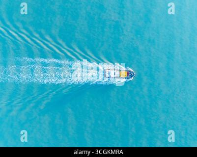 A lone boat moves across the wide blue ocean creating a foamy white wake as it sails calmly on the vast water. Stock Photo