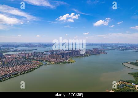 A large city with many buildings extends along the wide lake in Wuhan China under a bright blue sky with white clouds. Stock Photo
