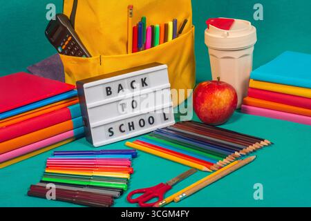 School supplies, backpack and lightbox showing back to school message on turquoise background Stock Photo
