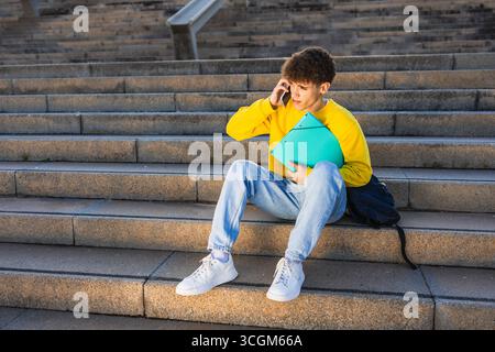 College student talking on smartphone while sitting on stairs outdoors Stock Photo