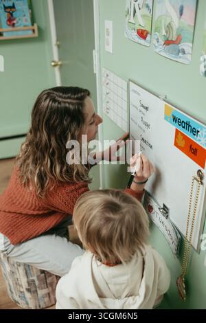 Teacher writing on whiteboard with student in montessori classroom Stock Photo
