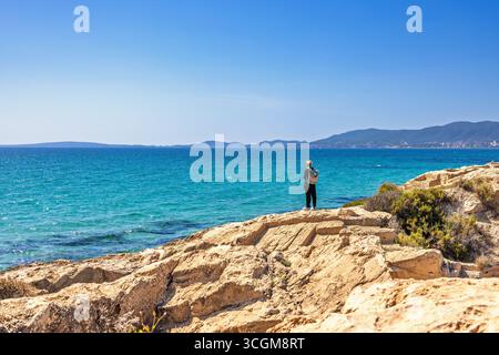 Alone young woman standing on a rock by the mediterranean sea a sunny summer day Stock Photo