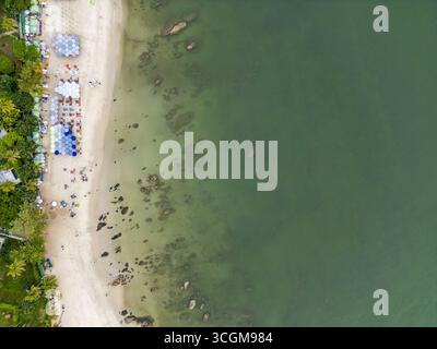 Aerial view of the beach edged with trees and umbrellas meeting the sea with rocks, Hua Hin, Prachuap Khiri Khan, Thailand. Stock Photo