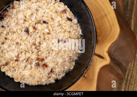 porridge with dried berries in a black bowl , cooking instant oatmeal porridge, closeup, top view Stock Photo