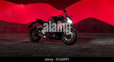 Sportbike on a street at night with red light trail behind it. Long exposure side view of Honda CBR 650R sport motorcycle with custom venom livery. Stock Photo