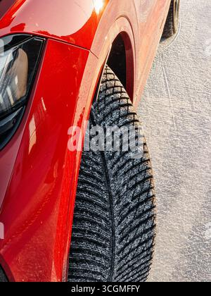 Winter tires on red car. Close-up image of tire thread covered with thin layer of snow. Stock Photo