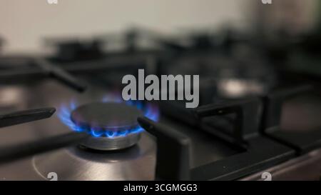 Blue flames emit from a gas stove burner, illuminating a kitchen workspace with a warm glow. Stock Photo