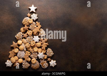 Cookies in different shaped of Christmas tree on brown background. Xmas festive greeting card. Holiday traditional food. Top view. Copy space. Stock Photo