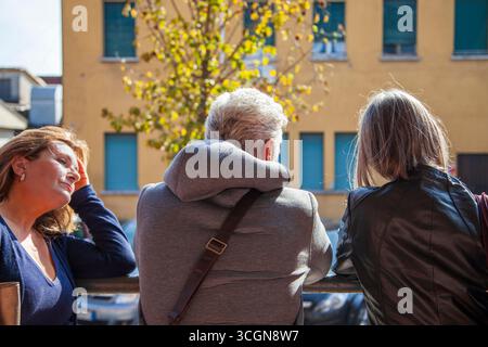 Three middle-aged commuters standing leaning on a railing and looking at a building while waiting for the bus Stock Photo