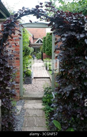A tranquil garden pathway leads through greenery and brick, inviting exploration of the well-maintained landscape and cozy surroundings. Stock Photo