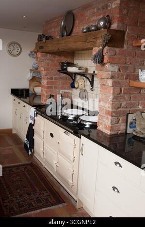 A vintage kitchen features a cream stove, black countertops, exposed brick, and wooden shelves for a cozy vibe. Stock Photo