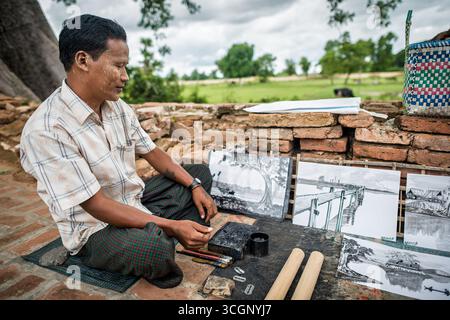 Yadana Hsemee Pagoda Complex Local Artist Creating Ink Drawings Inwa Myanmar | INWA, Myanmar — A local artist sketches ink drawings on stone slabs amid the brick ruins of the Yadana Hsemee Pagoda Complex in Apyin Sanyar Village. The ruined compound, west of the old Ava Palace, sits within the Inwa Ancient Cultural Heritage Zone, an area of brick stupas and image halls left in ruins after the 1839 Ava earthquake. Craft traditions like lacquerware and ink drawing remain part of daily life along the Inwa heritage circuit. Stock Photo