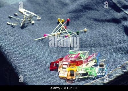 Sewing pins, safety pins and quilting clips scattered on blue denim fabric - tools for joining two parts of a product. Preparing for stitching clothes Stock Photo