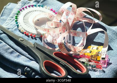 Sewing kit at home for repair and DIY projects. Scissors, pins, quilting clips and tape measure on denim. Symbol of practical living and money saving Stock Photo