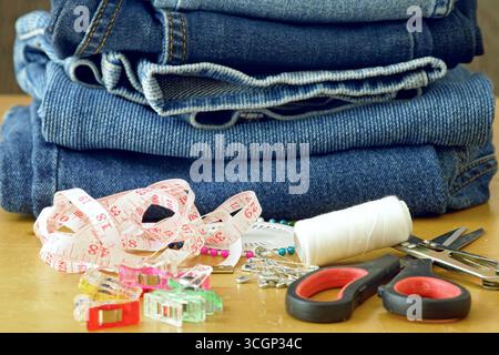 Professional tailoring supplies with folded denim jeans, measuring tape and sewing tools. Concept of fashion alteration, clothing repair, DIY crafting Stock Photo