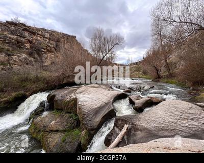 water of flowing river falling through the rocks in the valley among the mountains on a cloudy day Stock Photo