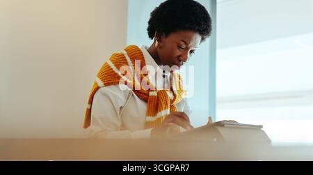 A focused woman engrossed in her work on a tablet, embodying concentration and productivity in a modern setting. Her thoughtful expression and relaxed Stock Photo