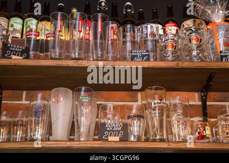moskow russia, 25.04.2019 Empty beer glasses with various logos and bottles display on wooden shelves in a bar against a brick wall. Stock Photo