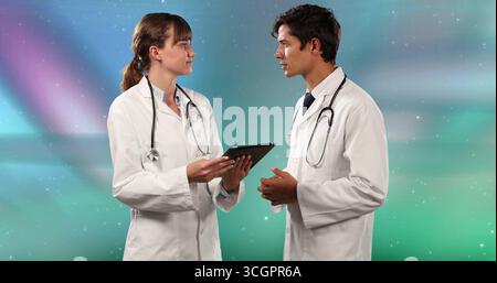 Two doctors wearing white coats holding tablet and discussing in studio, with two stethoscopes Stock Photo