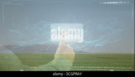 Reaching hand wearing green sleeve tapping BIG DATA button over crop field, digital interface Stock Photo
