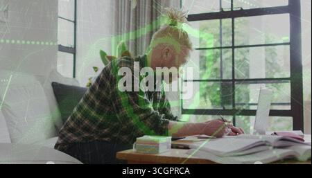 Writing man with top knot using laptop and notebook at home living room table, holding pen Stock Photo