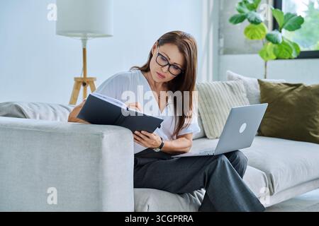 Middle aged serious woman working on c with laptop notepad Stock Photo