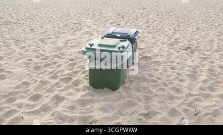 Green and black plastic waste containers buried in yellow sand on the beach. Ostend, Belgien. Stock Photo