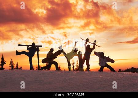 Silhouettes of one skier and four snowboarders in different funny poses against a colorful sunset sky. Winter holidays at ski resort Stock Photo