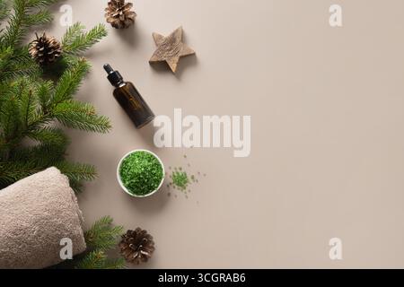 Christmas Spa concept with cosmetic aroma oil, pine cones, evergreen branches on beige background. Winter holiday for body care and wellness. View fro Stock Photo