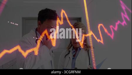Two doctors wearing lab coats analyzing data in hospital corridor, with clipboard and line graphs Stock Photo