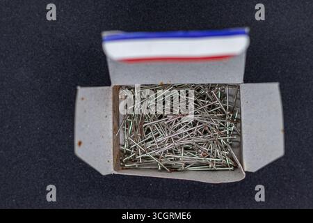 Open Cardboard Box Filled with Metal Office Pins on Black Surface Stock Photo