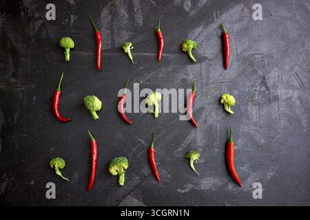 Minimalistic flat lay of fresh broccoli and red chili peppers arranged in a geometric pattern on a dark textured background. Perfect for healthy food, Stock Photo