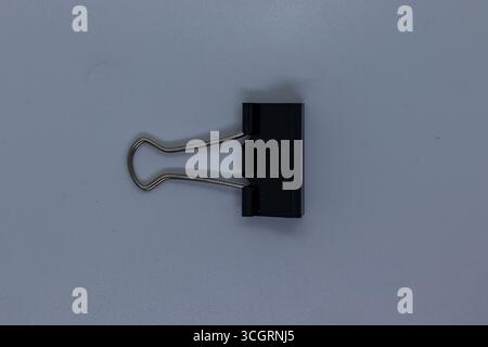Simple Black Binder Clip with Silver Handles on Clean White Surface Stock Photo