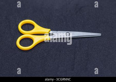 Small Yellow Handled Scissors with Stainless Steel Blades on Black Surface Stock Photo