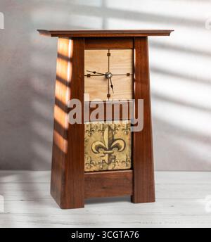 Mantle clock made of walnut and maple wood with fleur de lis inset on table with light coming through window blinds Stock Photo