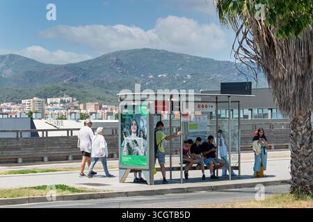 Viladecans. Barcelona - August 29, 2025: Several groups of people, including young people on their mobile phones and an elderly couple, wait at a bus Stock Photo