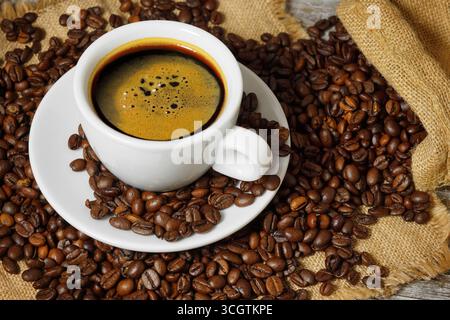 Coffee cup and roasted coffee beans in a burlap sack on a wooden rustic table close up view on rustic background. Stock Photo