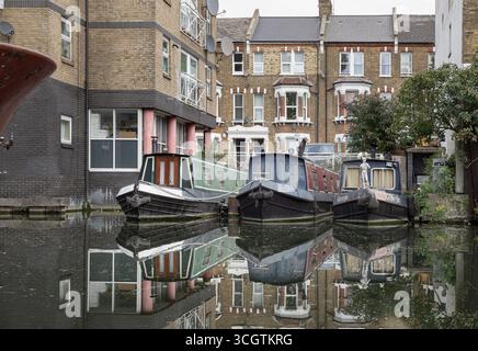 London, UK - Aug 23, 2025 - Picturesque scene of a dock for three narrowboats situated between an Edwardian-style terrace of houses. View of reflectin Stock Photo