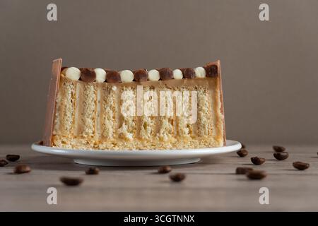 Close-up of a perfectly layered vanilla sponge cake slice with creamy layers and decorative chocolate topping, served on a white plate with scattered Stock Photo