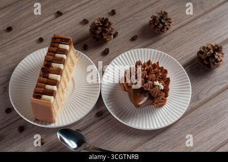 Two decadent desserts on white plates with pinecones and scattered coffee beans on a wooden table, evoking a cozy autumn atmosphere Stock Photo