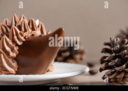A whimsical chocolate hedgehog shaped dessert with piped frosting spikes on a white plate, set against a rustic backdrop of pinecones and warm wooden Stock Photo