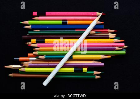 A variety of colored pencils in different shades are scattered on a black surface. The vibrant colors and unique arrangements highlight the tools of c Stock Photo