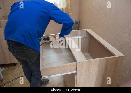 man gathers furniture with his back wrapped, assembling drawers installing sliding mechanisms Stock Photo