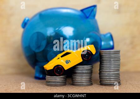 Yellow Toy Car on Coin Stacks with Blue Piggy Bank. Savings Concept Stock Photo