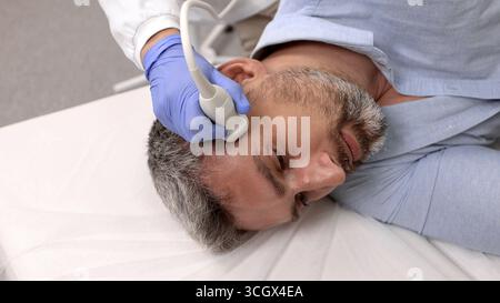 Experienced ultrasound specialist carefully analyzes structure of neck vessels of handsome patient using modern sonographic device in hospital Stock Photo