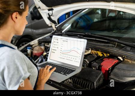 Female auto mechanic using laptop to inspect vehicle in workshop. Car performance graphs. Stock Photo
