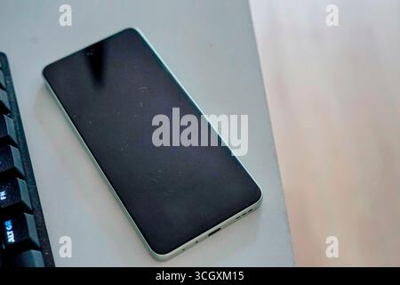 A modern smartphone with black screen placed on a desk beside a keyboard technology your text place work job online unplagued turned off  Stock Photo
